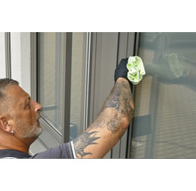 Mann mit Tattoos reinigt Fenster mit einem Tuch