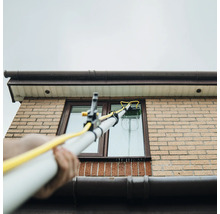 Fensterreinigung mit Teleskopstielbürste an einem Haus