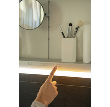Detailansicht eines Spiegelschranks mit Beleuchtung und einem Finger, der einen Schalter berührt.