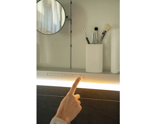 Detailansicht eines Spiegelschranks mit Beleuchtung und einem Finger, der einen Schalter berührt.