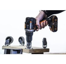 Eine Hand hält einen Akkuschrauber der Marke Worx beim Anbringen einer Lenkrolle an einem Holzbrett.