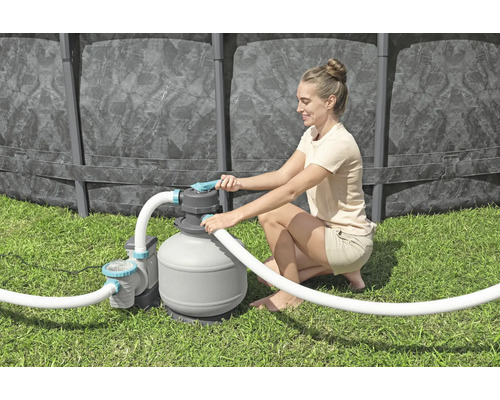 Frau bedient eine Sandfilteranlage für einen Pool im Garten.