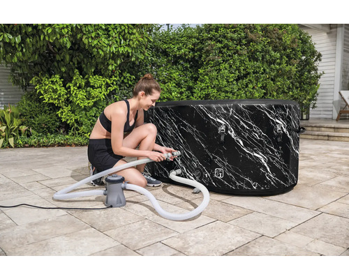 Frau schliesst auf der Terrasse einen aufblasbaren Whirlpool mit Marmormuster an eine Pumpe an