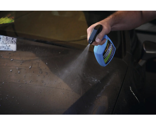Eine Person sprüht Autowachs aus einer Sprühflasche auf ein Auto.