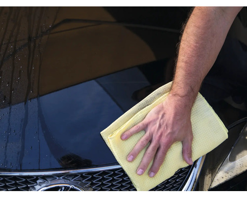 Ein Mann wischt ein Auto mit einem Tuch.