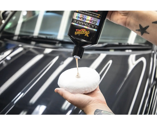 Eine Person trägt Polierpaste von Meguiars auf ein Polierpad auf, um ein Auto zu polieren.