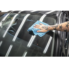 Ein Mann wischt die Windschutzscheibe eines Autos mit einem Mikrofasertuch ab.