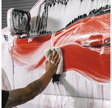 Person wäscht Auto mit Reinigungsmittel und Tuch