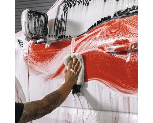 Person wäscht Auto mit Reinigungsmittel und Tuch