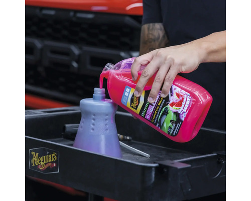 Eine Person gießt Autoshampoo in einen Behälter für Autowäsche. Meguiar''s Logo