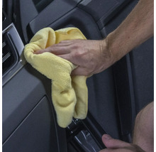 Eine Hand wischt mit einem gelben Tuch ein Auto sauber.