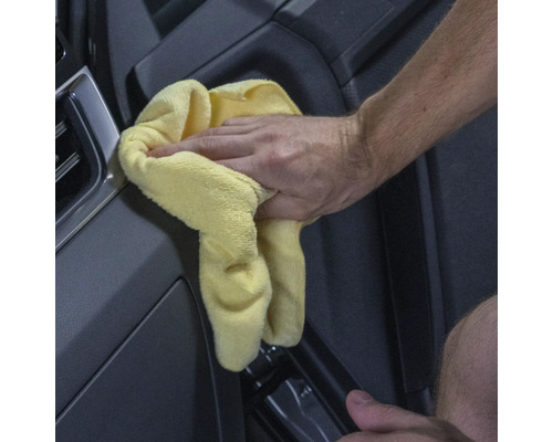 Eine Hand wischt mit einem gelben Tuch ein Auto sauber.