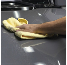 Eine Hand poliert ein graues Auto mit einem Tuch.