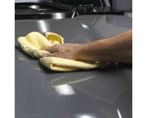 Eine Hand poliert ein graues Auto mit einem Tuch.