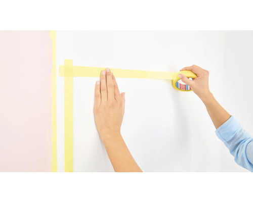 Person klebt Malerkrepp an eine Wand