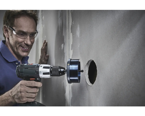 Mann bohrt mit einer Lochsäge ein Loch in eine Wand