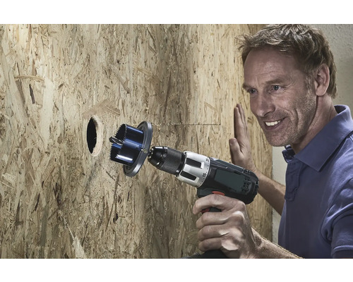 Mann bohrt mit einer Lochsäge ein Loch in eine Holzplatte.