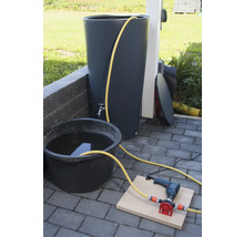 Regenwassertonne mit Wasserhahn, Eimer mit Wasser, Bohrmaschine und Pumpe auf Steinboden
