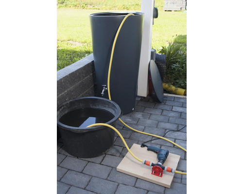 Regenwassertonne mit Wasserhahn, Eimer mit Wasser, Bohrmaschine und Pumpe auf Steinboden
