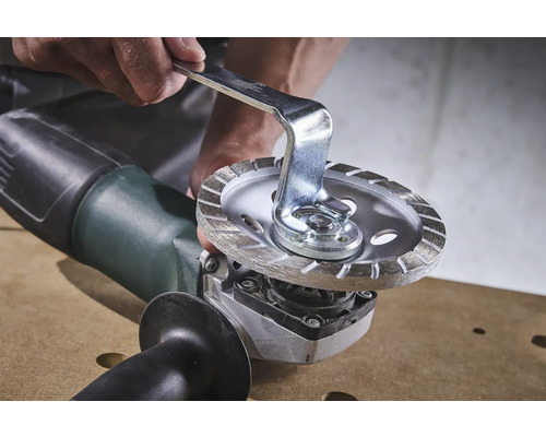 Person wechselt Trennscheibe an einem Winkelschleifer mit Gabelschlüssel.
