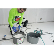 Handwerker mischt Silikatfarbe mit einem Farbmischer in einem Eimer