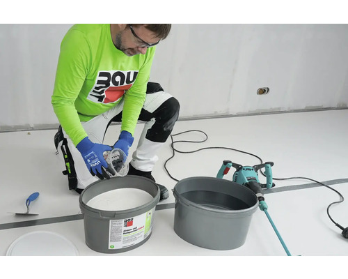 Handwerker mischt Silikatfarbe mit einem Farbmischer in einem Eimer