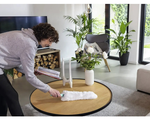 Frau wischt Staub von einem Holztisch in einem Wohnzimmer mit Staubwedel