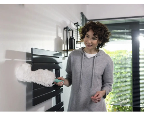 Frau reinigt Heizkörper mit Staubwedel