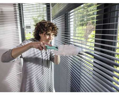 Frau reinigt Jalousien mit Staubwedel