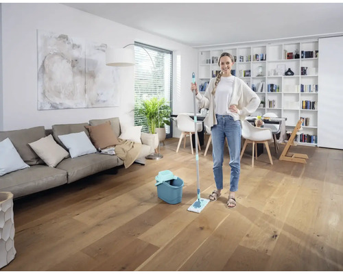 Frau mit Mopp und Eimer in einem hellen Wohnzimmer auf Holzboden