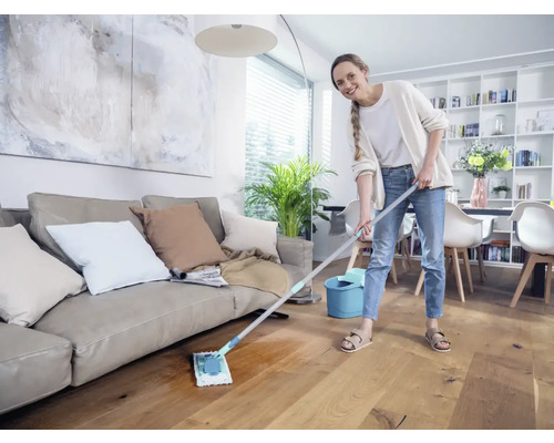 Frau wischt Holzboden im Wohnzimmer mit Wischmopp und Eimer.