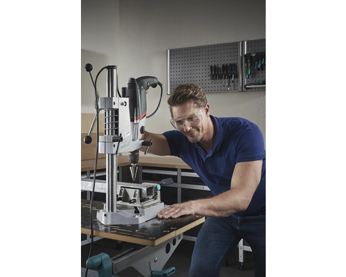 Mann mit Schutzbrille beim Bohren mit einer Tischbohrmaschine in einer Werkstatt