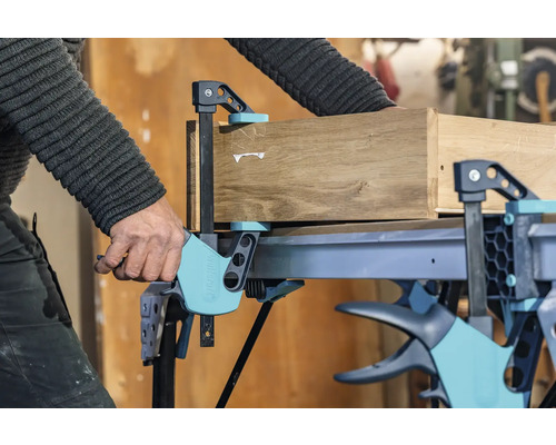 Eine Werkbank mit einer Schraubzwinge fixiert ein Holzstück.