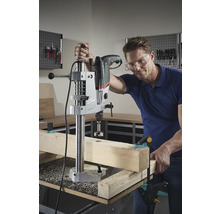 Mann bohrt mit einer Tischbohrmaschine ein Loch in ein Holzstück. Er trägt eine Schutzbrille.