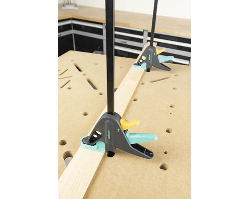 Zwei Einhandzwingen fixieren ein Holzbrett auf einer Werkbank.