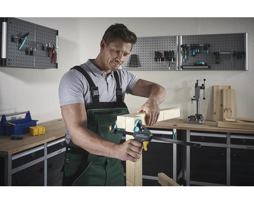 Mann fixiert Holzstücke mit einer Einhandzwinge in einer Werkstatt