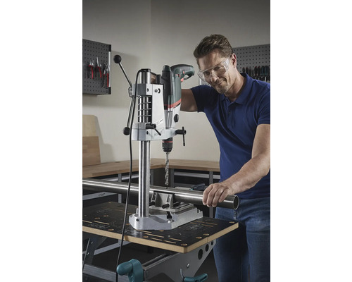 Mann bohrt mit einer Tischbohrmaschine ein Rohr auf einer Werkbank