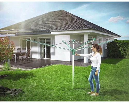 Frau bedient eine Wäschespinne im Garten vor einem Wohnhaus.