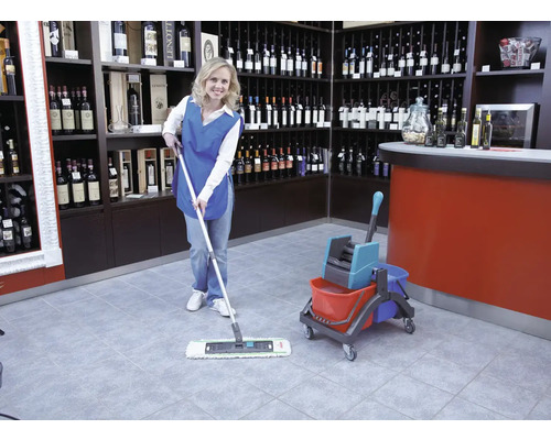 Reinigungskraft wischt mit einem Mopp und Eimer einen Fliesenboden in einem Weinladen.