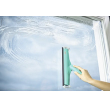 Hand wischt mit einem Fensterwischer eine Glasfläche sauber