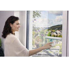 Frau putzt Fenster mit einem Fensterwischer für streifenfreie Sauberkeit