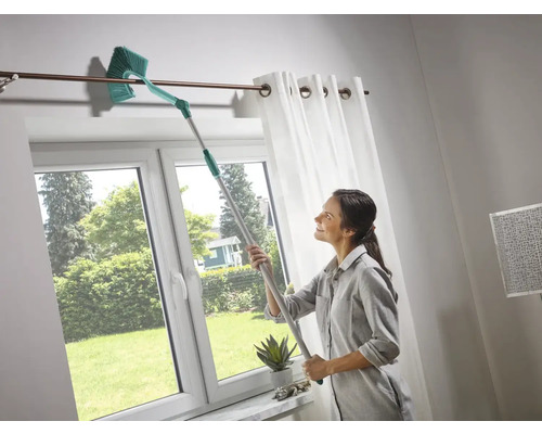 Frau reinigt Vorhangstange mit Teleskop-Staubwedel in einem hellen Raum