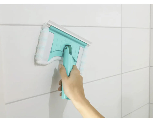 Hand die einen Fensterwischer mit Mikrofaserbezug an einer gefliesten Wand verwendet