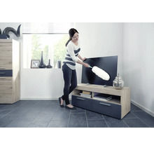 Frau wischt Staub von einem Fernseher mit einem Staubwedel in einem Wohnzimmer.