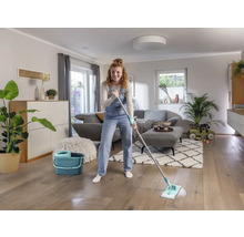 Frau wischt Holzboden mit einem Mopp und einem Eimer in einem Wohnzimmer