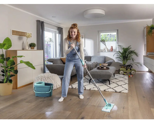 Frau wischt Holzboden mit einem Mopp und einem Eimer in einem Wohnzimmer