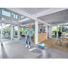 Frau wischt Boden im hellen Wohnzimmer mit Wischmopp und Eimer