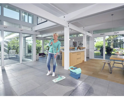 Frau wischt Boden im hellen Wohnzimmer mit Wischmopp und Eimer