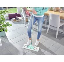 Frau wischt Fliesenboden mit einem Mopp im Wohnzimmer