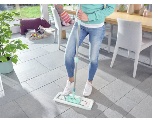 Frau wischt Fliesenboden mit einem Mopp im Wohnzimmer